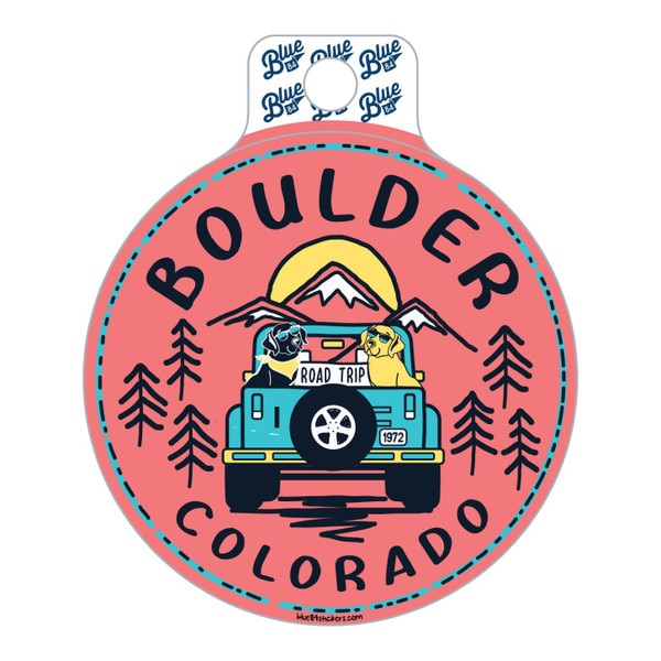 This is a circular coral colored sticker that has black text. On each side, there are 3 black linework evergreens. The dogs on the back are black and gold. The jeep and decor around the rim are teal.