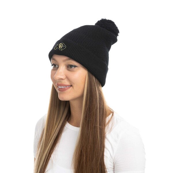 Black CU Boulder waffle-knit beanie with embroidered gold logo and pom detail, shown on a person wearing a white shirt at an angle