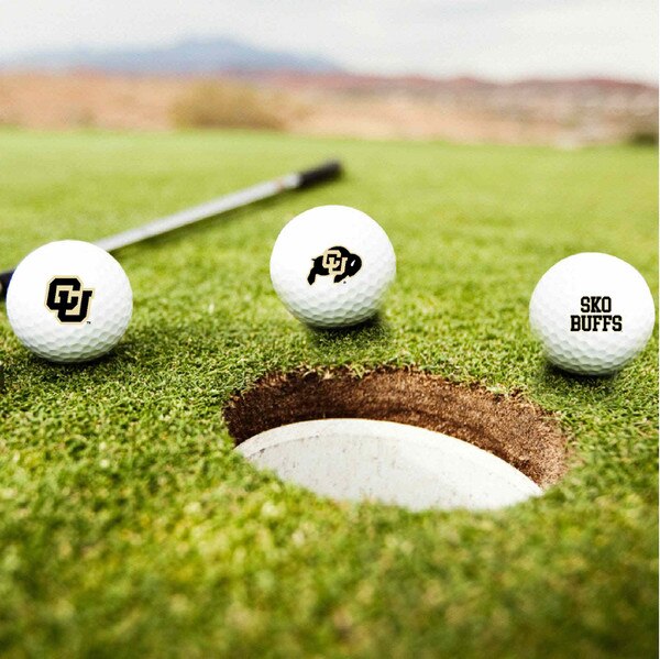Three University of Colorado golf balls with CU logos and “SKO BUFFS” text on a putting green near a hole